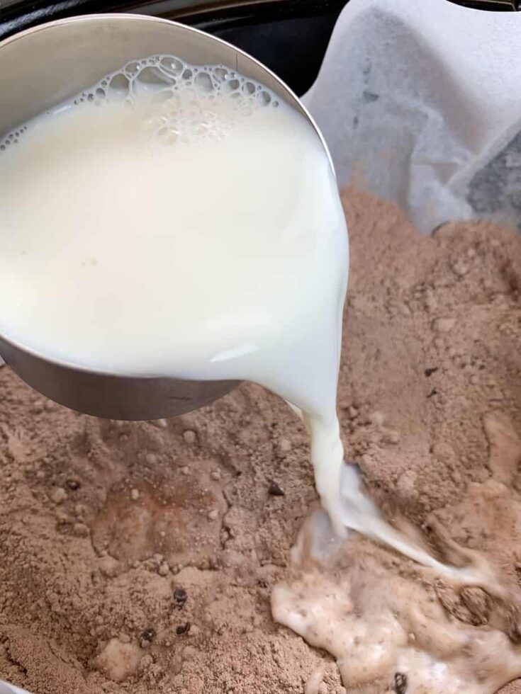 Pouring milk into a slow cooker with chocolate cake mix