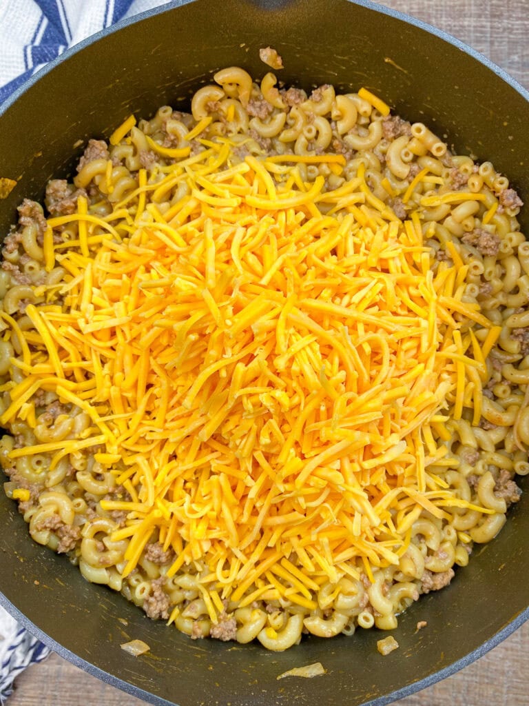 Shredded cheddar cheese in a pan with noodles and beef. 