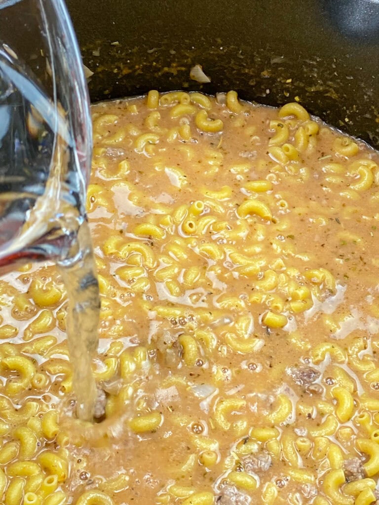 Water and macaroni noodles in a pan with ground beef. 