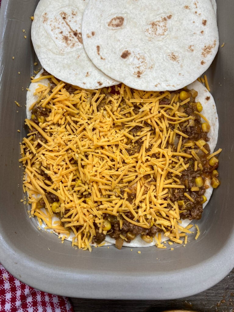 Layering mexican casserole in a baking dish with tortillas and meat and cheese. 