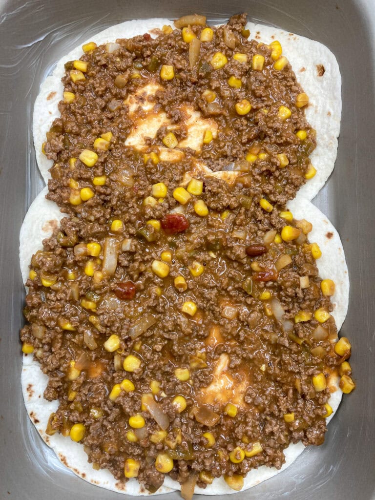 Spreading ground beef mixture over tortillas in a baking dish. 