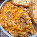 Cheesy hamburger casserole on a plate with two slices of thick garlic bread.