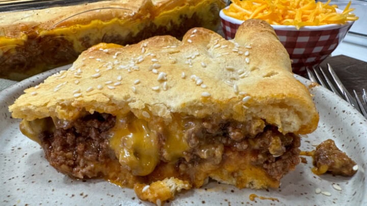 Sloppy joe crescent roll with cheese on a white plate. The plate is on top of a wooden plate.