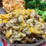 Hamburger mac and cheese on a dish with a biscuit and broccoli.