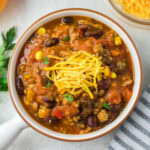 A bowl of pumpkin turkey chili with some shredded cheese on top.