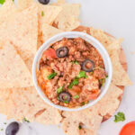 taco dip in a white bowl with tortilla chips