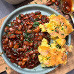 Baked beans on a plate with some cornbread.