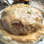 A hamburger steak with gravy on top of mashed potatoes.